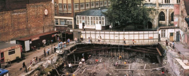 Archeological dig site beneath a bridge surrounded by buildings