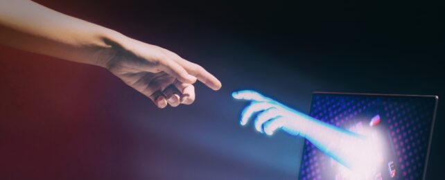 A human hand reaching out to a fake hand extending from a laptop screen.